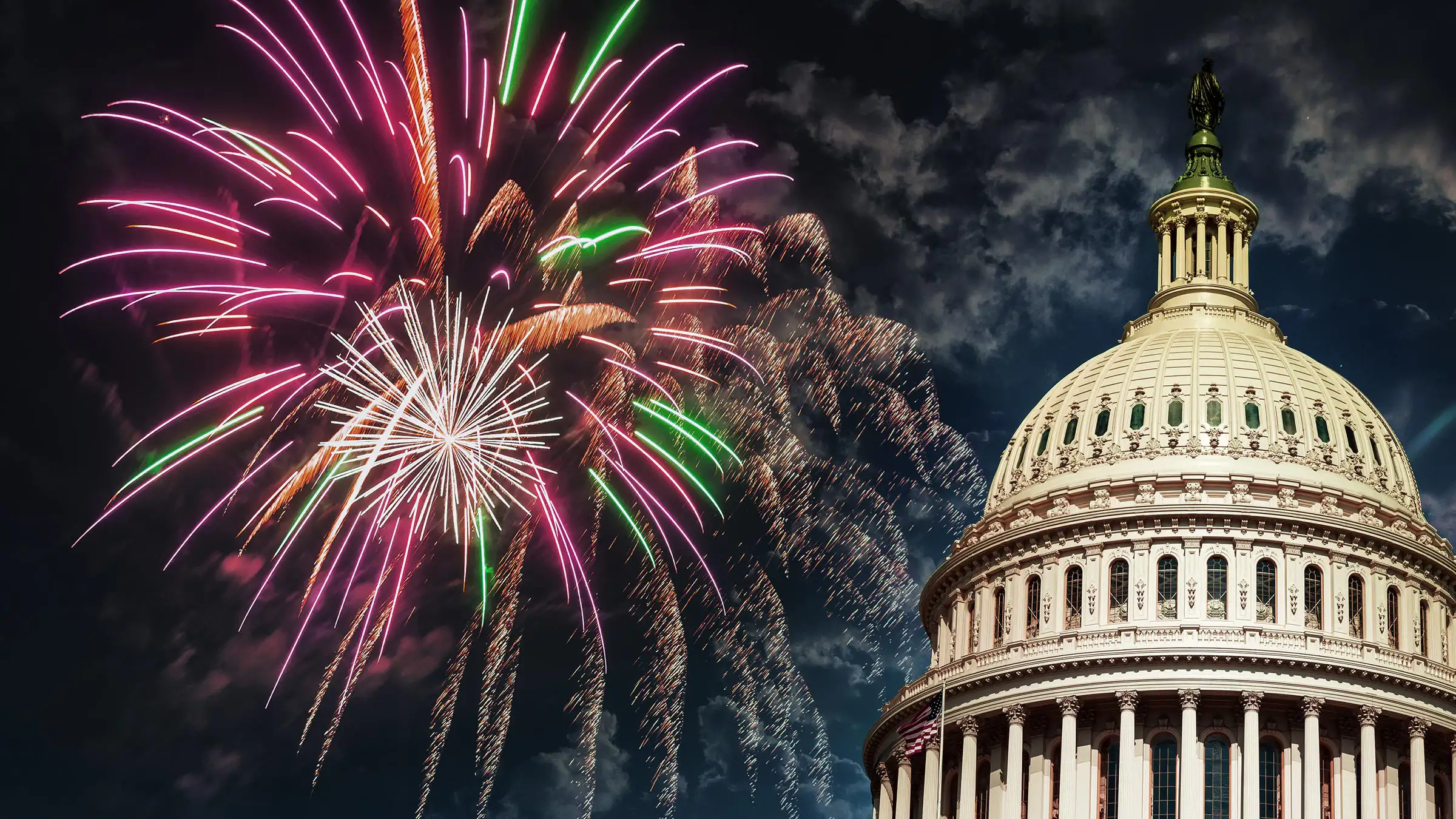 Celebration-Banner Colorful fireworks burst in the night sky above the U.S. Capitol dome, which is partially visible on the right. The fireworks display includes vibrant red, green, and pink colors.